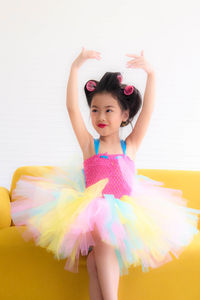 Portrait of cute girl sitting on yellow pink sofa and wearing colorful dress