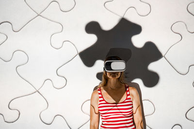 Unrecognizable young female in casual outfit and virtual reality goggles exploring cyberspace with puzzle pieces