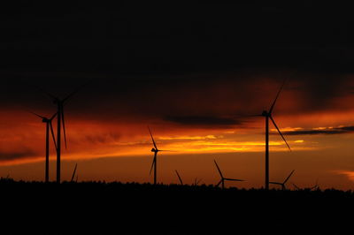 Silhouette wind turbines on landscape against sky during sunset