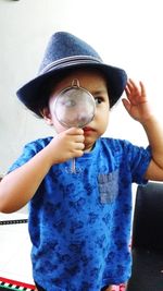 Portrait of boy holding hat against blue wall