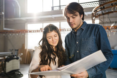 Smiling colleagues discussing document while standing at industry