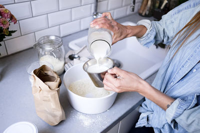 Midsection of woman pouring ingredient in bowl at kitchen counter