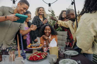 Happy friends giving gifts to excited young woman while celebrating birthday in back yard