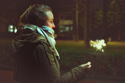 Side view of woman looking at sparkler at night