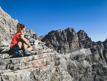 Full length of woman sitting on rocky mountain