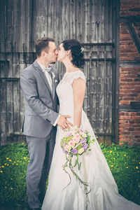 Bride and groom kissing while standing on grassy field