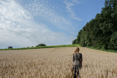 Rear view of woman standing on field against sky