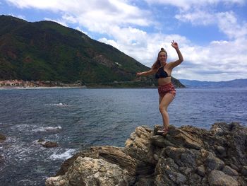 Woman gesturing while standing on rocky shore against mountain