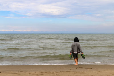 Rear view of woman walking on beach against sky