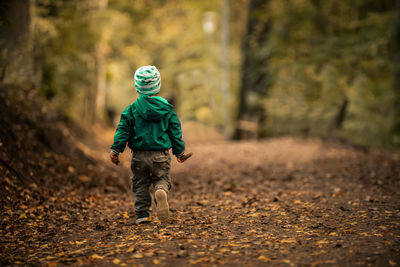 Rear view of boy walking in forest during winter