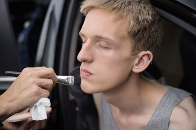 Cropped hands applying make-up on male friend sitting in car