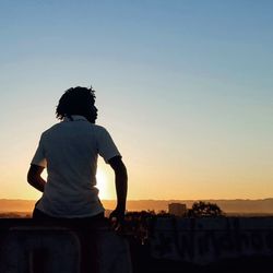 Rear view of woman sitting against sky during sunset