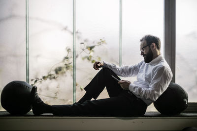 Businessman sitting on window sill reading text messages