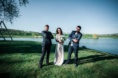 Full length of smiling young couple on grass against sky