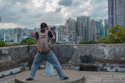 Rear view of man looking city through coin-operated binoculars