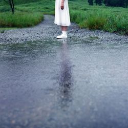 Low section of woman standing by puddle on street