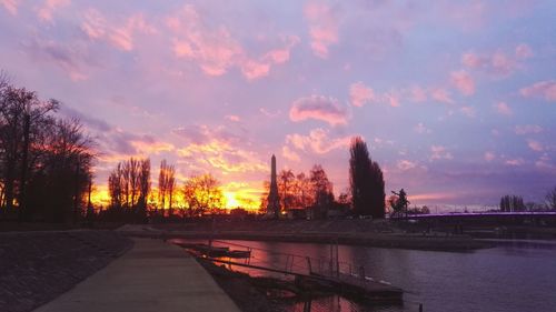 Bridge over river by buildings against sky during sunset