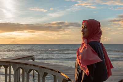 Boy standing by sea against sky during sunset