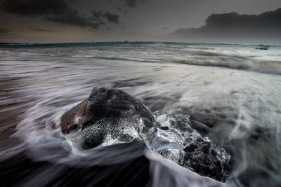 Close-up of sea wave splashing on beach against sky