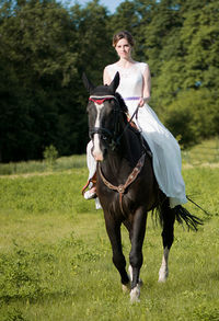 Bride riding horse on grassy field