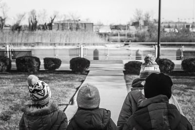 Rear view of people sitting on riverbank against sky