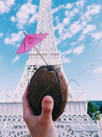 Cropped hand holding coconut against replica eiffel tower