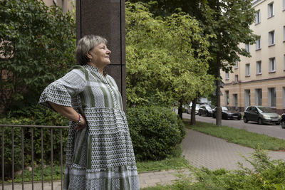 Real smiling female woman in yard of modern building. green trees around. copy space for text