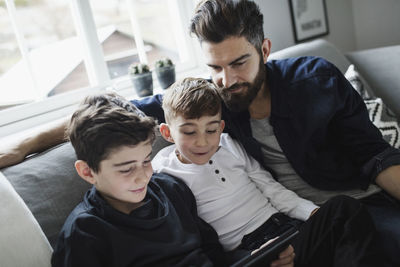 Tilt shot of father and son looking at boy using digital tablet in living room