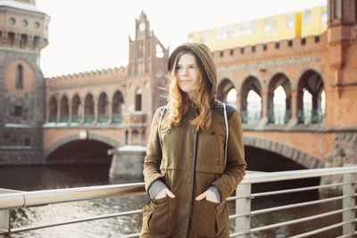 Beautiful young woman with hands in pockets standing on footbridge