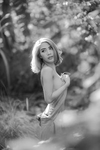 Side view of topless young woman looking away while standing against trees