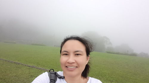 Portrait of smiling woman on field against foggy weather