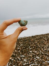 Close-up of hand holding pebble against beach