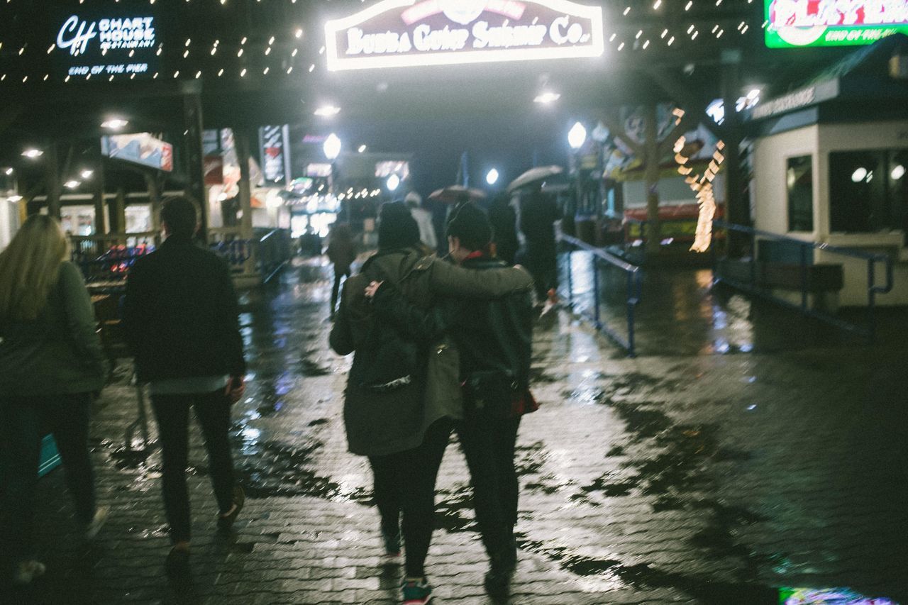 PEOPLE WALKING ON WET ILLUMINATED NIGHT