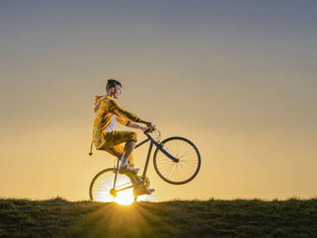 Man riding bicycle on field against sky during sunset