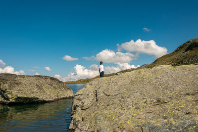 Man standing on rocks by sea against blue sky