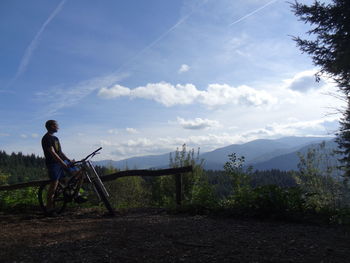 Man with bicycle on cliff against sky