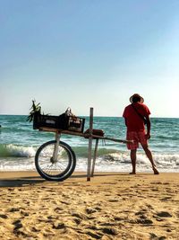 Rear view of man standing by hand cart at beach against sky