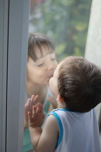 Close-up of siblings kissing on window