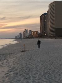 Modern buildings by sea against sky during sunset