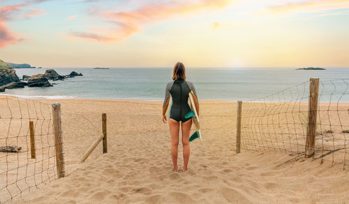 Surfer woman with wetsuit and surfboard looking at the sea