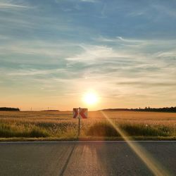 Road amidst field against sky during sunset