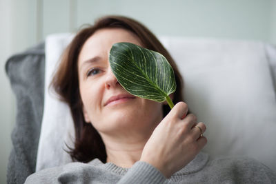 Portrait of woman holding leaf at home