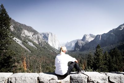 Rear view of woman sitting on rock against mountains