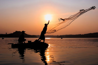 Rear view of silhouette man standing in sea against sky during sunset