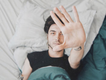 High angle view of man gesturing stop while lying on bed at home