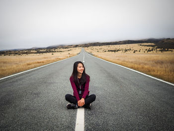 Portrait of woman sitting on road against sky