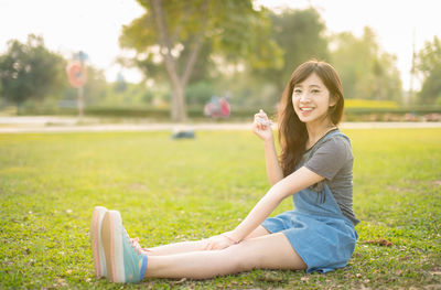 Full length portrait of smiling young woman sitting on field at park