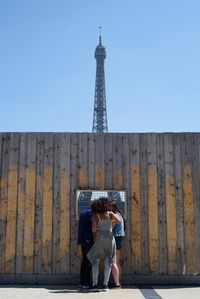 Man and woman sitting against tower against clear blue sky