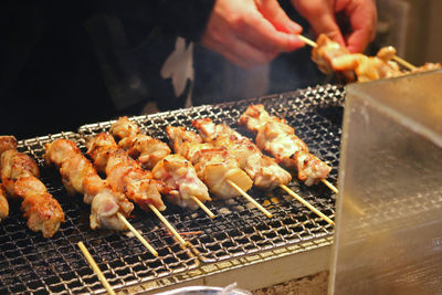 Cropped hands preparing meat on barbecue grill