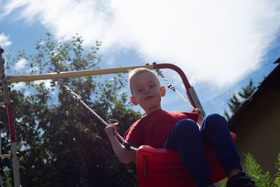 Low angle view of man sitting on swing against sky